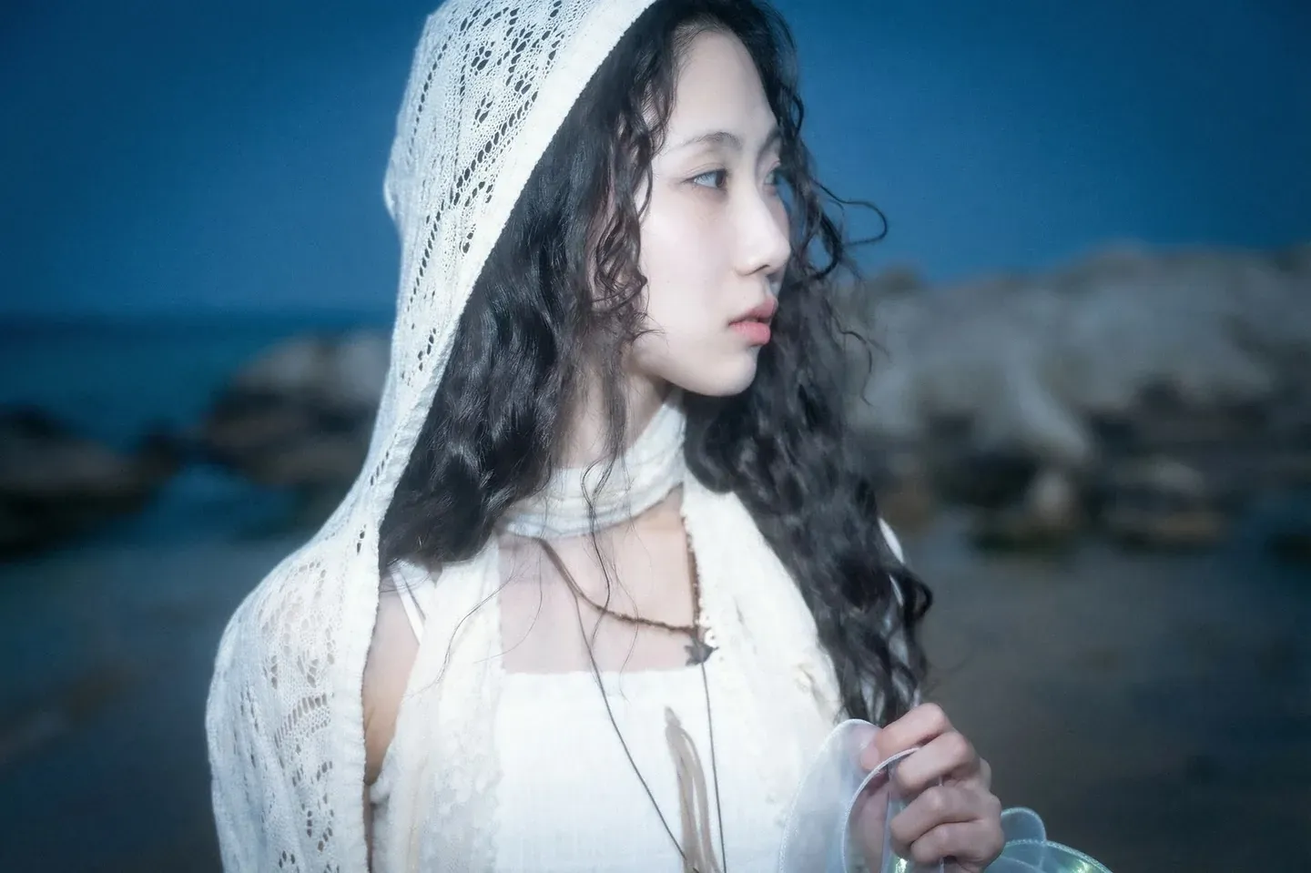Gyuri in a lace hood in front of rocks by a blue sea